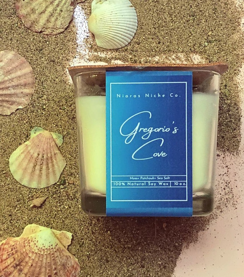Gregorio's Cove candle by Niaras Niche Co., 10 oz natural soy wax, scent: Moss, Patchouli, Sea Salt, surrounded by seashells.