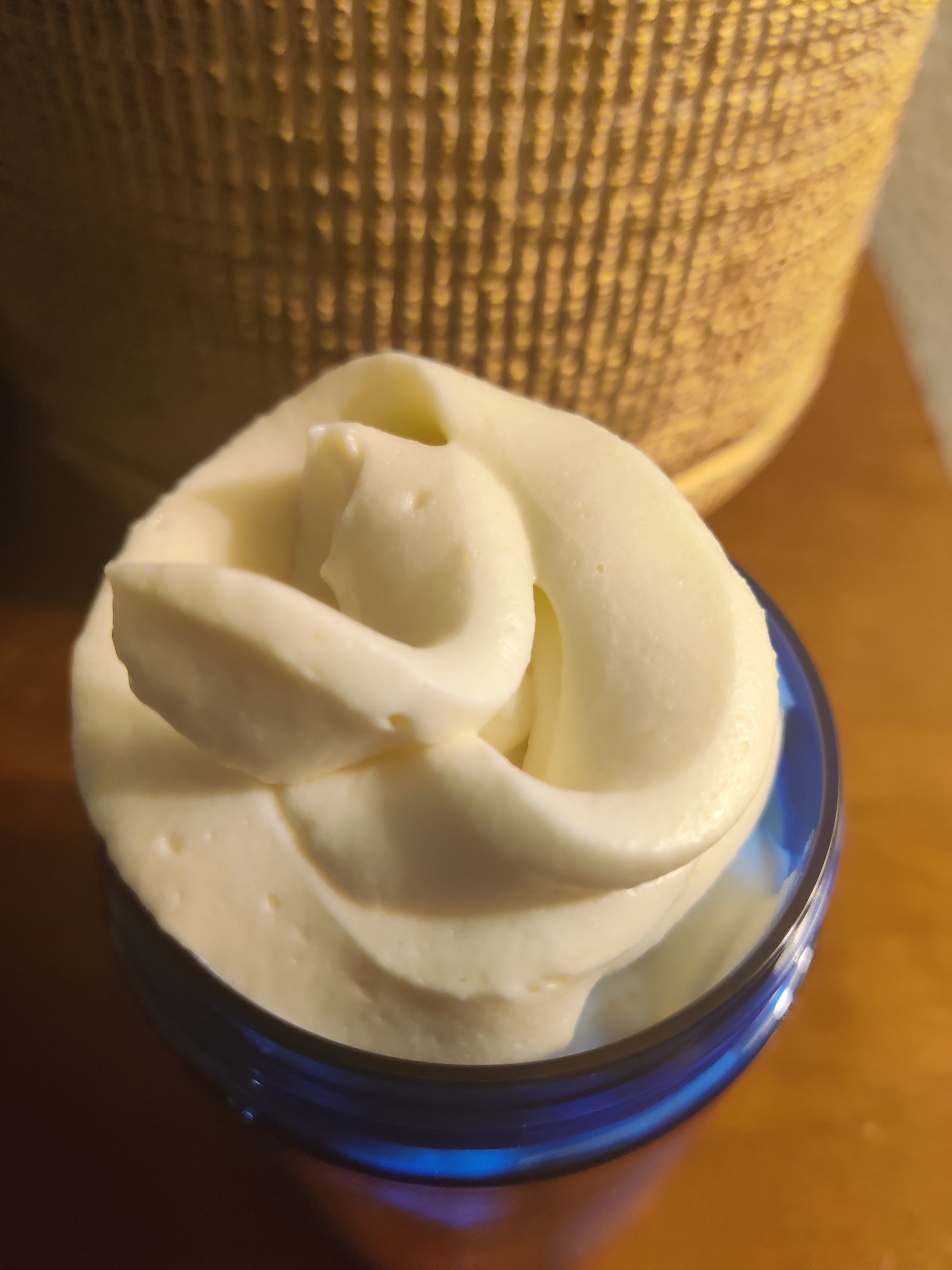 Close-up of creamy white body butter in a blue jar, topped with a decorative swirl for a luxurious look.