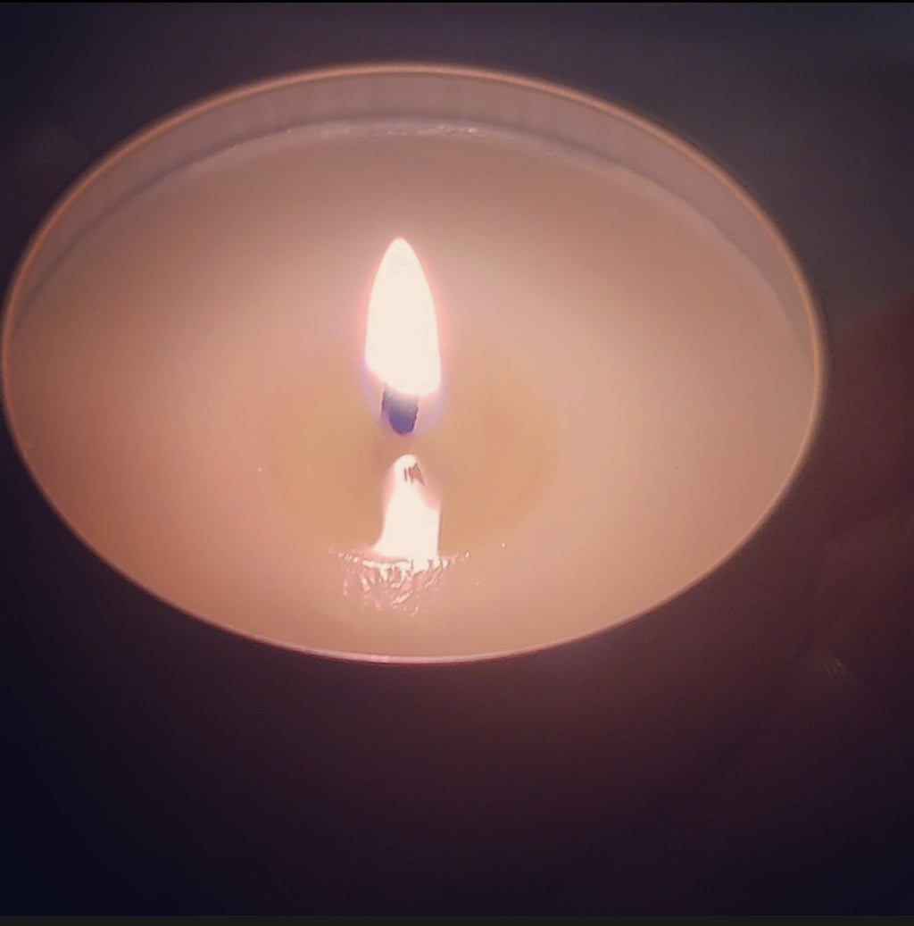 Close-up of a lit white candle with a blue wick, showcasing a warm, flickering flame in a minimalist holder.