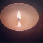 Close-up of a lit white candle with a blue wick, showcasing a warm, flickering flame in a minimalist holder.